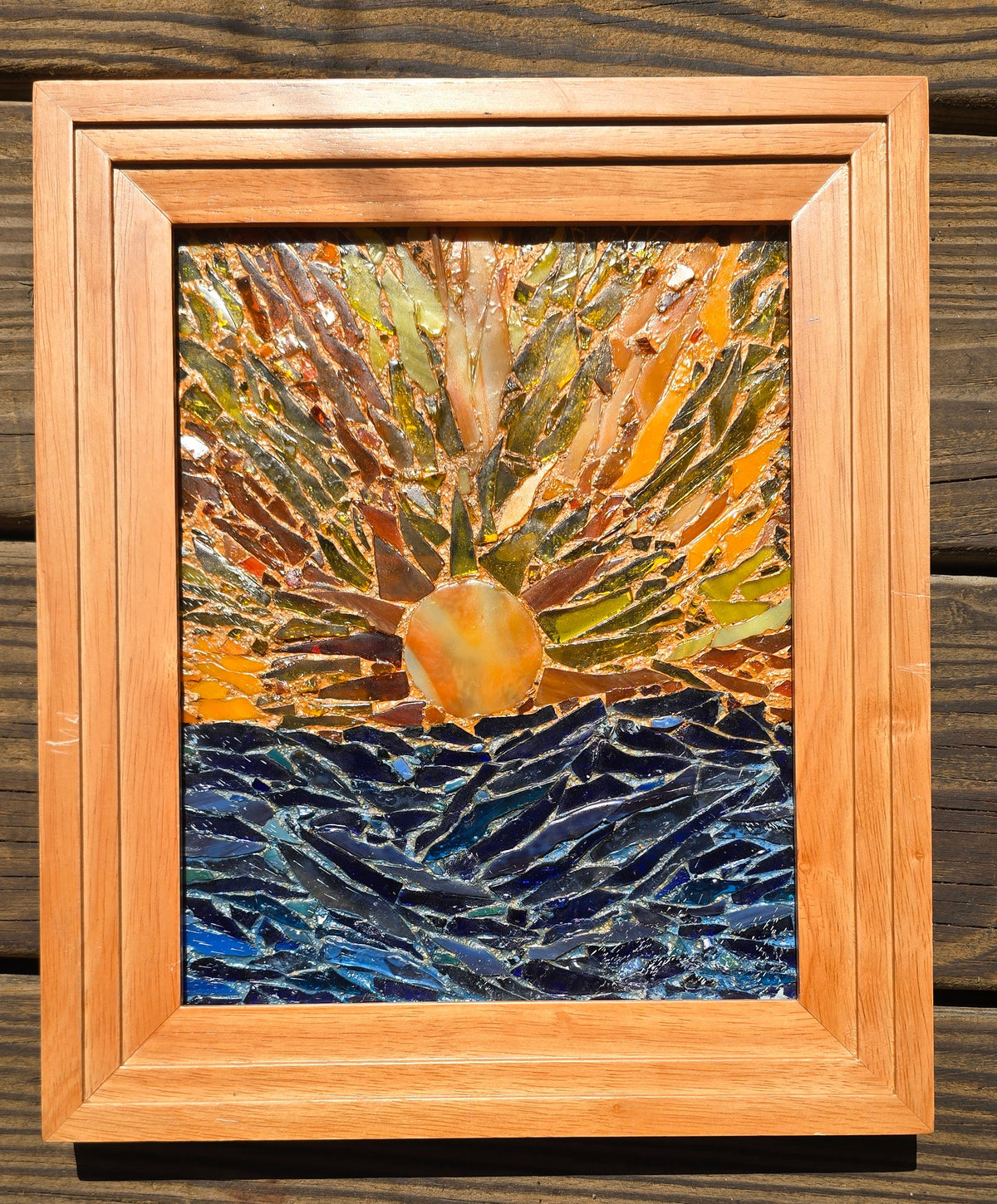 Handcrafted glass on glass mosaic depicting Sunset Beach Hawaii sunset, warm sun tones blending into deep ocean blues, framed 8x10 artwork with grout made from real Sunset Beach sand