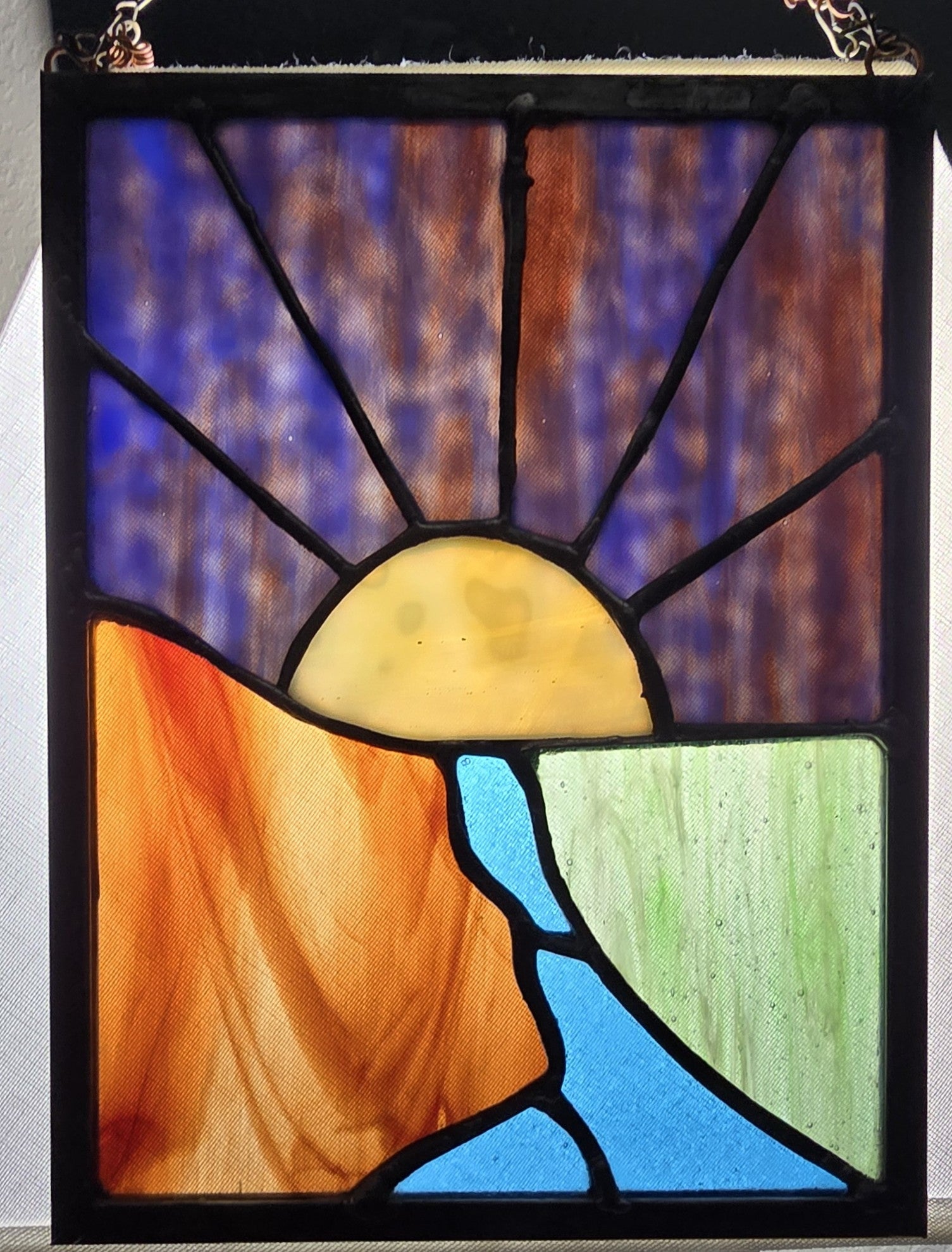 Stained glass panel with a sun and landscape design on a white background